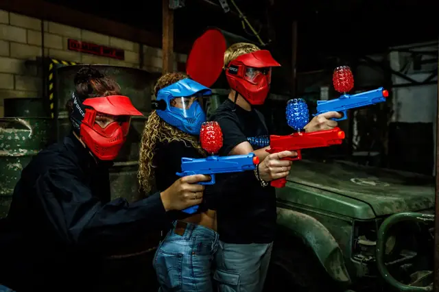 Trois joueurs masqués, lanceurs à billes de gel en main, prêts à jouer